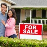 Hispanic couple outside home with for sale sign