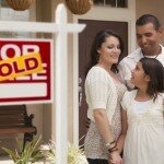 Hispanic Mother, Father and Daughter in Front of Their New Home with Sold Home For Sale Real Estate Sign.