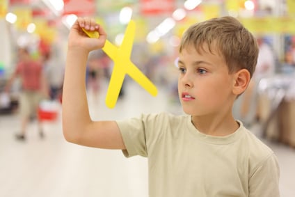 little boy holding yellow boomerang toy, standing in shop