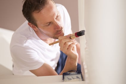 Young male painter painting indoor with paintbrush and white paint do it yourself