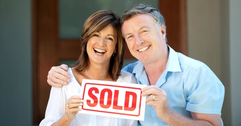 Happy mature couple holding sold sign