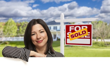 Hispanic Woman Leaning on White in Front of Beautiful House and Sold For Sale Real Estate Sign