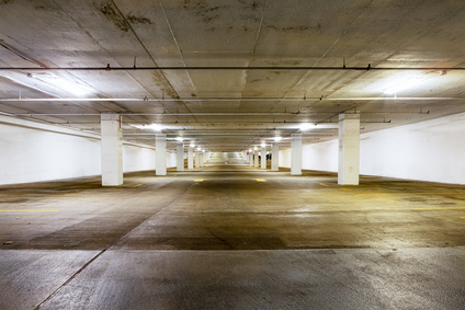 Large grungy empty undercover parking area viewed down the length with receding perspective lit by overhead strip lights