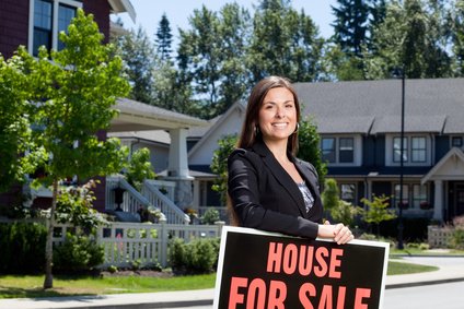 Professionally dressed real estate woman outside with a house for sale sign