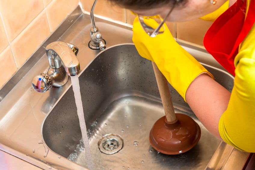 cleaning clogged pipes in the kitchen sink with a plunger