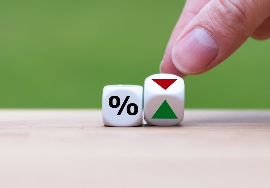 Hand is turning a dice and changes the direction of an arrow symbolizing that the interest rates are going down or vice versa