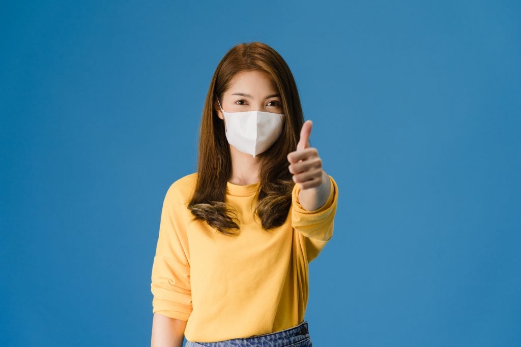 Young Asia girl wearing medical face mask showing thumb up with