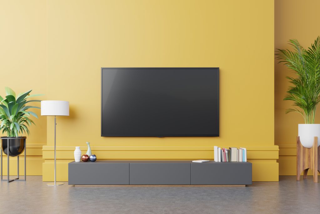 TV on cabinet in modern living room with lamptableflower and plant on yellow wall background