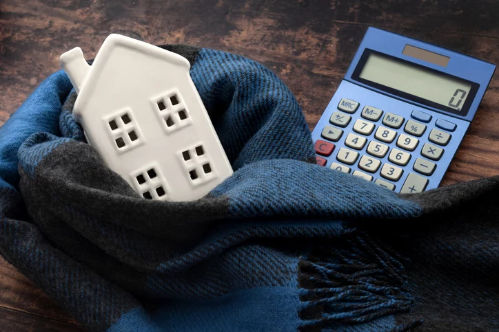 Warming efficiency of a residence and calculate heating costs concept with digital calculator small house wrapped in warm wool neck scarf on wood background