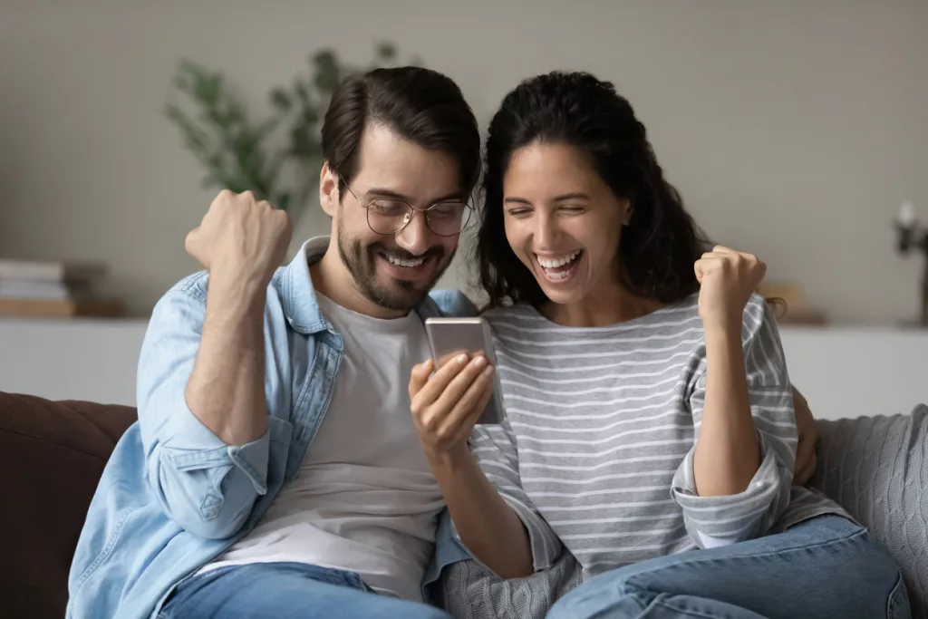 Excited joyful family couple using smartphone looking at screen