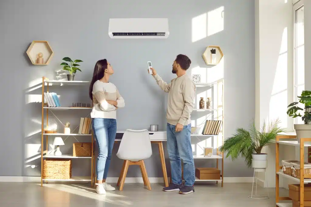 Young family couple setting up the temperature on the air conditioner in the living room